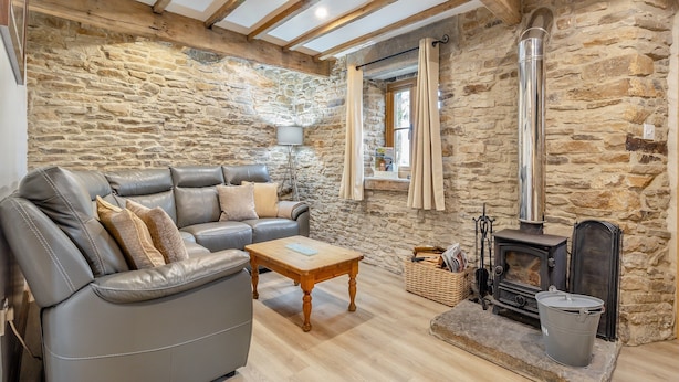 A cozy living room with a stone wall, a leather sofa, a wooden coffee table, and a fireplace. - 3 bedroom accommodation in Cutthorpe, near Chesterfield (Cutthorpe, near Chesterfield)