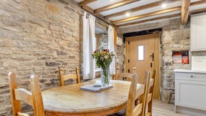 A rustic dining area with a stone wall, wooden ceiling beams, and a round wooden table with chairs. - 3 bedroom accommodation in Cutthorpe, near Chesterfield (Cutthorpe, near Chesterfield)