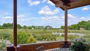 A covered outdoor seating area with a table and chairs, overlooking a grassy field and a body of water. - 3 bedroom accommodation in Burgh le Marsh, near Skegness (Burgh le Marsh, near Skegness)