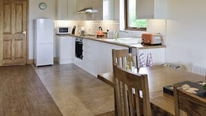 A modern kitchen with white cabinets, a wooden ceiling, a built-in oven, a microwave, a toaster, and a window with a view of greenery. - 3 bedroom accommodation in Burgh le Marsh, near Skegness (Burgh le Marsh, near Skegness)