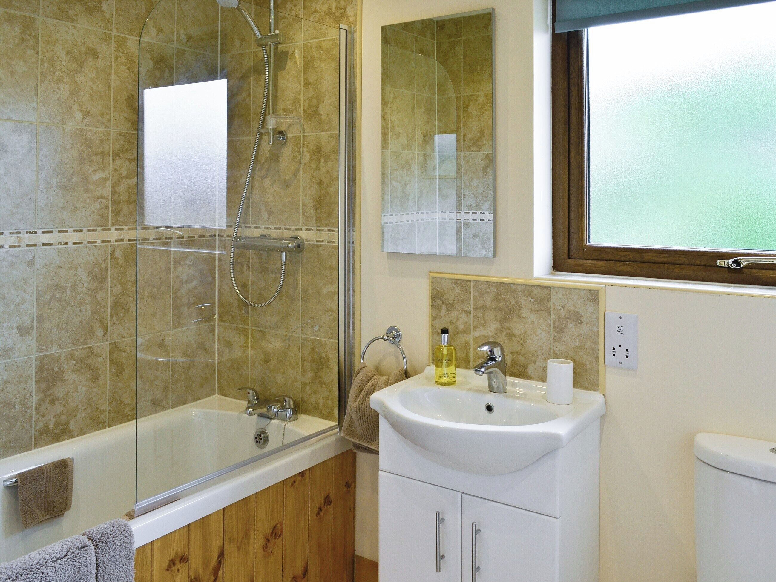 Un baño con cabina de ducha de vidrio, un lavabo con espejo y una ventana.