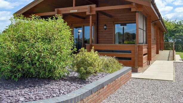 A wooden cabin with a porch, surrounded by landscaped greenery and gravel. - 3 bedroom accommodation in Burgh le Marsh, near Skegness (Burgh le Marsh, near Skegness)