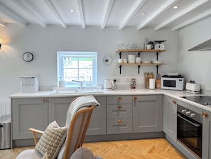 Een moderne keuken met grijze kastjes, een houten stoel, een raam en een spoelbak.