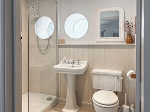 Et moderne badeværelse med en glasafskærmet brusebad, et væghængt håndvaskarrangement og et toilet.