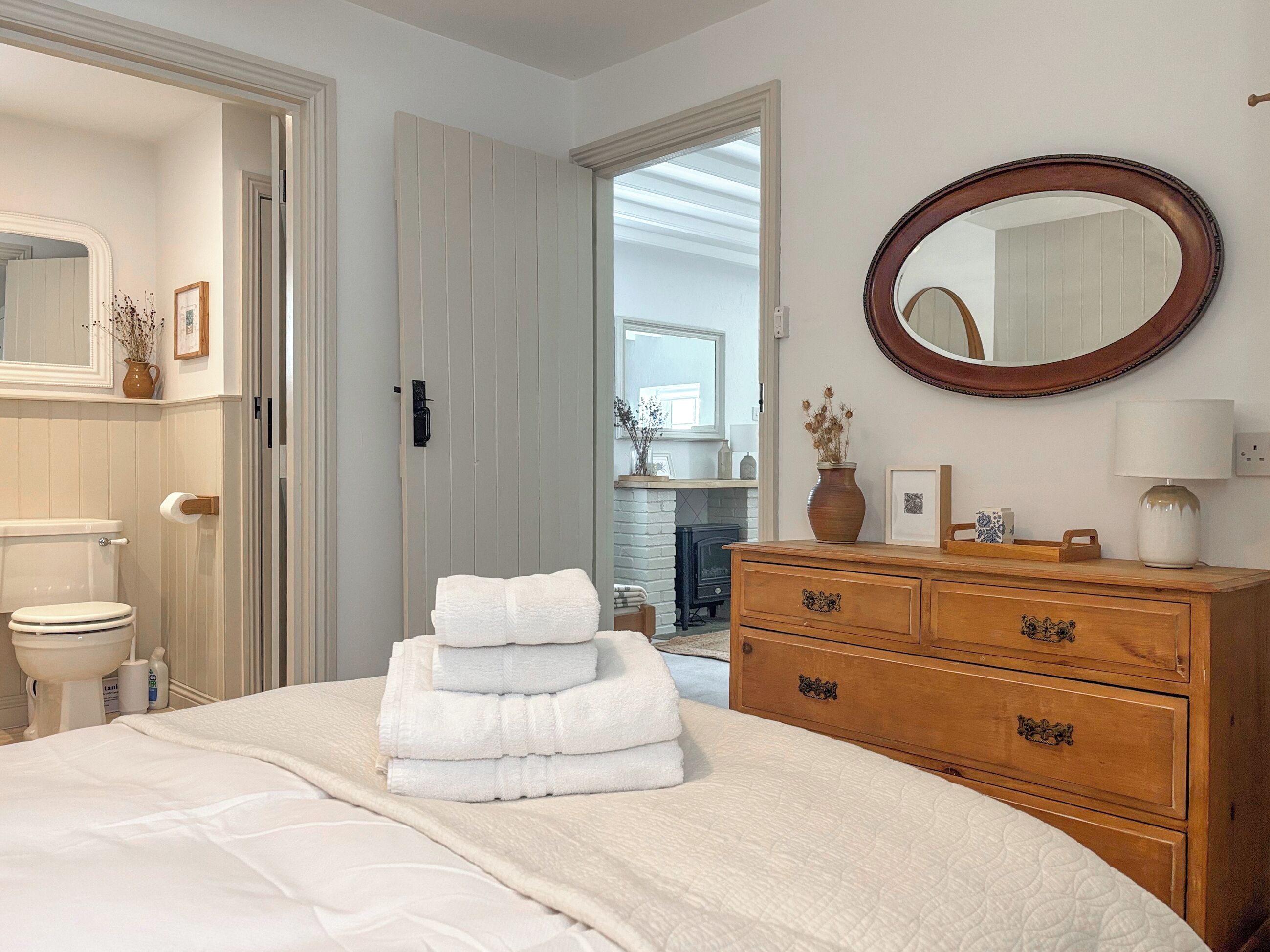 A bedroom with a bed, a wooden dresser, a mirror, and a bathroom visible through an open door.