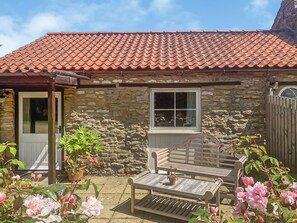 A stone building with a tiled roof, a wooden bench, and potted plants.