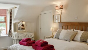 Une chambre d’hôtel avec un grand lit, une table de chevet avec une lampe, un miroir et une fenêtre avec des rideaux.