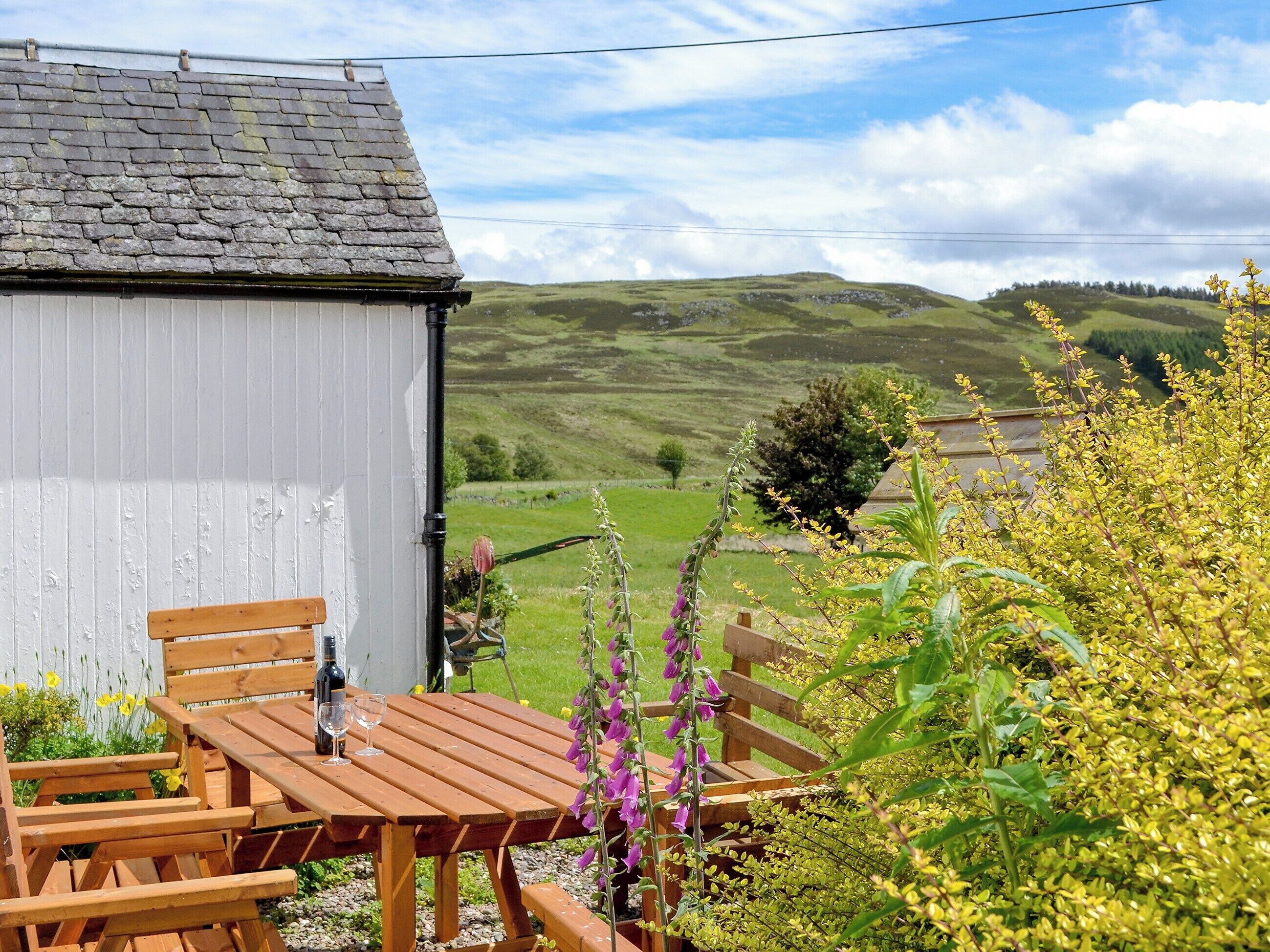 A wooden table and chairs outside a building with a view of green hills.