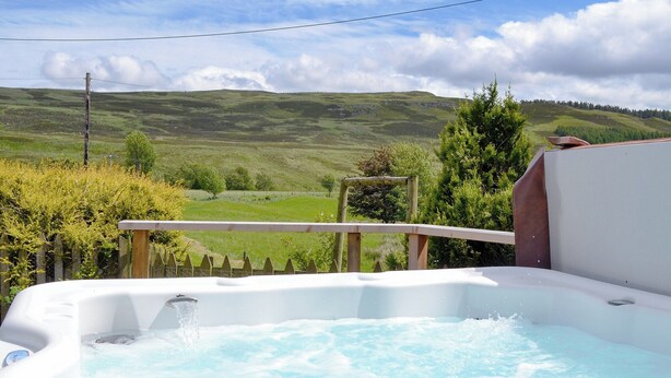 Un bain à remous avec une terrasse en bois et une vue sur des collines verdoyantes.