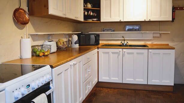 A kitchen with white cabinets, a wooden countertop, a sink, and a stove. - 3 bedroom accommodation in Brixham (Brixham)