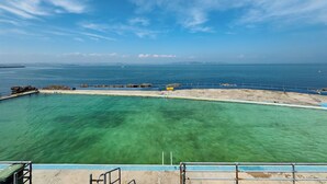 A clear view of a swimming pool with a blue border, a concrete deck area, and a distant view of the sea and sky. - 3 bedroom accommodation in Brixham (Brixham)