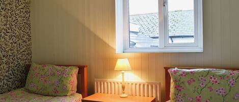 A bedroom with two beds, a nightstand, a lamp, and a window.