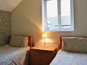Ein Schlafzimmer mit zwei Betten, einem Nachttisch, einer Lampe und einem Fenster.