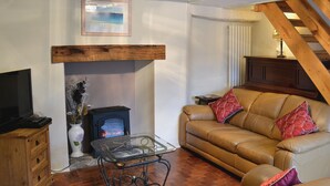 Ein gemütliches Wohnzimmer mit Kamin, Ledersofa und Fernseher auf einem Holzkasten.