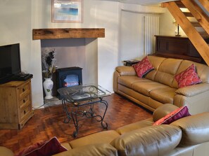A cozy living room with a fireplace, leather sofa, and a television on a wooden cabinet. - 3 bedroom accommodation in Brixham (Brixham)