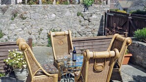 Eine Sitzgruppe im Freien aus Rattangeflecht mit Tisch, zwei Stühlen und einer Weinflasche.