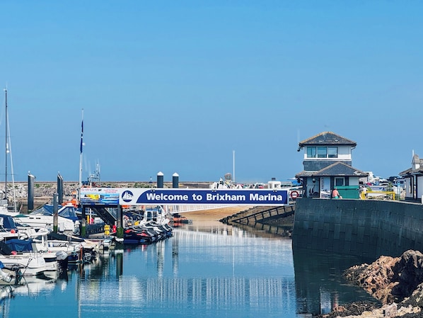 A marina with boats docked, a sign welcoming visitors to Brixham Marina, and a control tower.