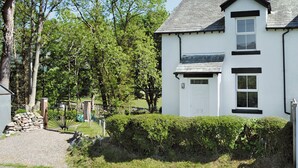 A two-story white house with a grey roof, a white door, and a small window on the ground floor. - 2 bedroom accommodation in Portinscale, near Keswick (near Portinscale)