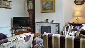 A living room with a television, a fireplace, a clock, and a sofa. - 2 bedroom accommodation in Portinscale, near Keswick (near Portinscale)