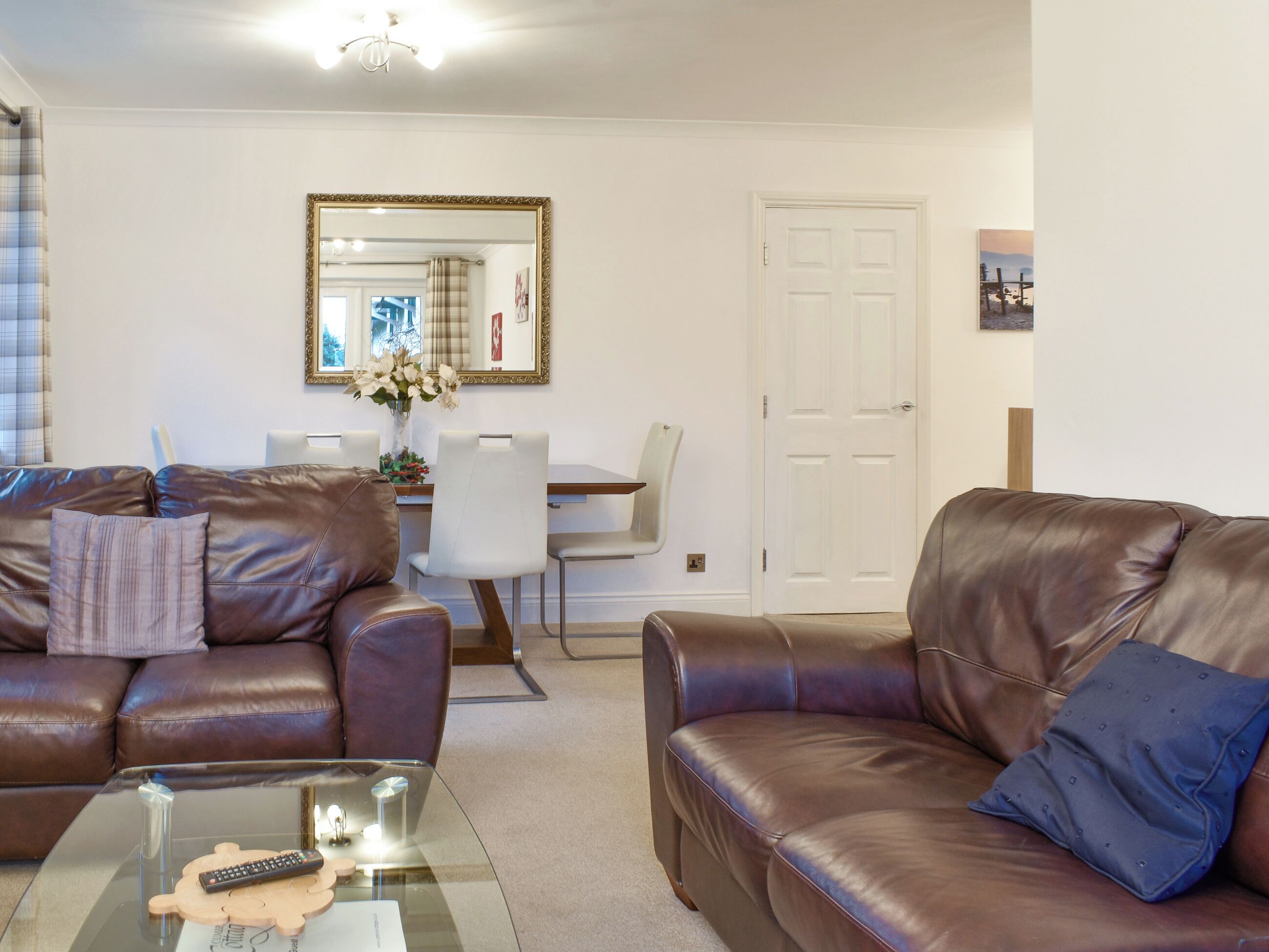 A living room with two brown leather sofas, a glass coffee table, and a dining area with a white table and chairs.