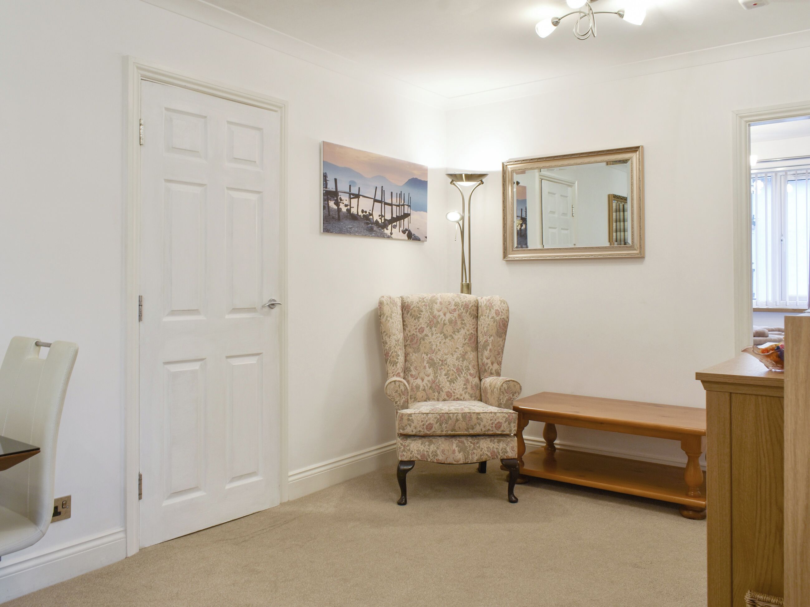 A room with a white door, a framed picture, a mirror, a chair, and a wooden bench.