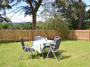 An outdoor dining area with a table set for four, surrounded by chairs, under a wooden fence.