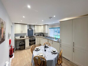 A compact kitchen with white cabinets, a microwave, and a dining area set for four with a table set for a meal. - 2 bedroom accommodation in Hulme End, near Hartington (Hulme End, near Hartington)