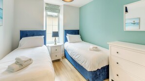 Et soveværelse med to senge, et natbord med lampe, en kommode og et vindue med rullegardiner.
