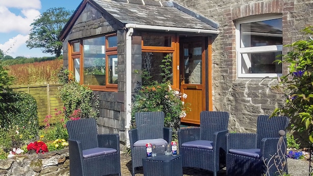 A stone building with a small porch, wicker furniture, and a garden with flowers and plants. - 2 bedroom accommodation in Carthamartha, near Launceston (Carthamartha, near Launceston)