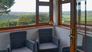 A corner room with two wicker chairs, a view of the countryside, and a door with a brass handle. - 2 bedroom accommodation in Carthamartha, near Launceston (Carthamartha, near Launceston)