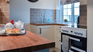 A modern kitchen with a wooden countertop, a sink, a stove, and a clock on the wall. - 2 bedroom accommodation in Harlyn Bay, near Padstow (Harlyn Bay, near Padstow)