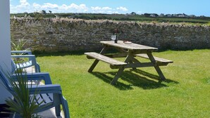 A picnic table with a bottle and glasses on it, set on a grassy lawn with a stone wall in the background. - 2 bedroom accommodation in Harlyn Bay, near Padstow (Harlyn Bay, near Padstow)