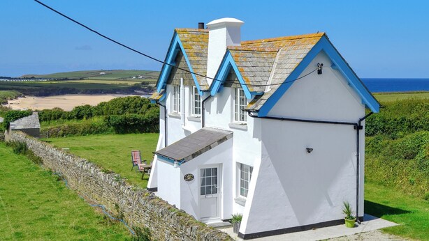 A white house with blue trim and a sloped roof, located on a grassy hill overlooking a beach and the sea. - 2 bedroom accommodation in Harlyn Bay, near Padstow (Harlyn Bay, near Padstow)
