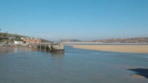 A coastal scene with a pier extending into calm waters, a sandy beach, and a backdrop of hills. - 2 bedroom accommodation in Harlyn Bay, near Padstow (Harlyn Bay, near Padstow)