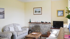 A living room with a stone fireplace, a sofa, a coffee table, and a television. - 3 bedroom accommodation in near Alnwick (near Alnwick)