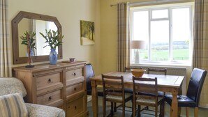 A dining area with a wooden table, chairs, a wooden dresser, a mirror, a vase with plants, and a window with curtains. - 3 bedroom accommodation in near Alnwick (near Alnwick)