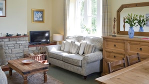 A cozy living room with a stone fireplace, a sofa, a wooden coffee table, and a dining table. - 3 bedroom accommodation in near Alnwick (near Alnwick)