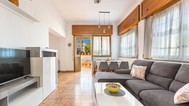 Un salon moderne avec un téléviseur à écran plat, un canapé gris et un coin repas à l’arrière-plan.