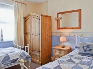 A bedroom with two beds, a wooden wardrobe, a bedside table with a lamp, and a mirror on the wall.