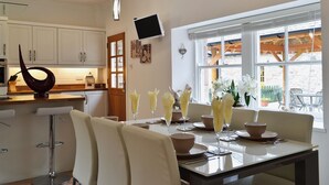 Una cocina moderna con armarios blancos, un comedor con mesa de vidrio y un ventanal con vistas al exterior.