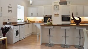 Una cocina moderna con armarios blancos, electrodomésticos de acero inoxidable y una isla central con taburetes de bar.