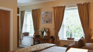 Un dormitorio con cama, mesita de noche, ventana con cortinas, radiador y lámpara fijada a la pared.