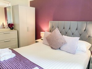 A neatly made bed with a tufted headboard, a bedside table with a lamp, and a wardrobe.