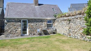 A stone house with a tiled roof, a chimney, and a small garden area with chairs. - 2 bedroom accommodation in Near Abersoch (Near Abersoch)