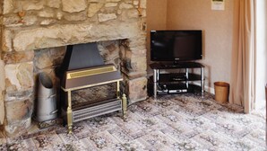 A stone fireplace with a television on a stand, a patterned carpet, and a curtain. - 2 bedroom accommodation in Near Abersoch (Near Abersoch)