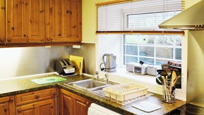 A kitchen with wooden cabinets, a dishwasher, a stove, and a window with blinds. - 2 bedroom accommodation in Near Abersoch (Near Abersoch)