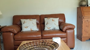 A brown leather sofa with two patterned pillows, a wooden coffee table with a decorative bowl, and a wooden cabinet in a living room.