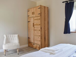Une chambre à coucher avec une grande armoire en bois, un fauteuil blanc recouvert de tissu et un lit avec une couette blanche.