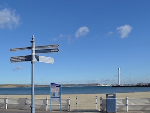 Ein Wegweiser mit mehreren Pfeilen, die zu verschiedenen Zielen zeigen, darunter 'Coast Path', 'Toiletten', 'Greenhill Gardens', 'Lodmoor Country Park', 'Bahnhof', 'Tourist Information Centre', 'Pavilion Theatre' und 'Hafen'.