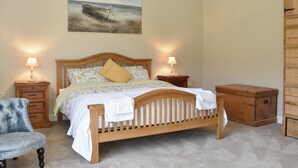 A bedroom with a wooden bed, two bedside tables with lamps, a chair, a wooden chest, and a painting on the wall.